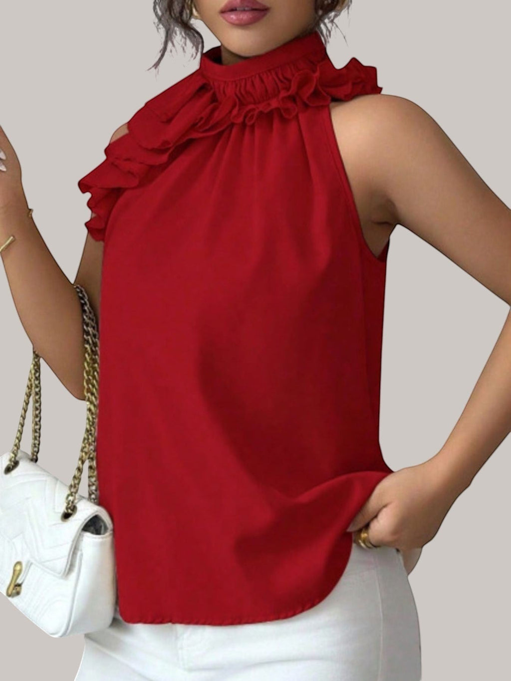 MICHEL red sleeveless top with a high ruffled neckline and button closure, worn by a model with a white handbag.